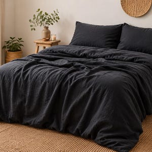 May include: A charcoal black duvet cover set featuring a textured fabric finish. The bedding includes a large duvet cover draped over a bed frame and two matching rectangular pillowcases, creating a uniform dark aesthetic for the sleeping space.