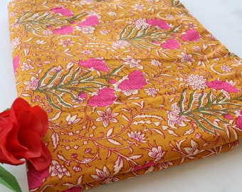 May include: A yellow fabric with a pink and white floral print. The fabric is folded and has a red rose in the foreground.