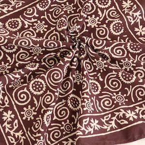 Peut inclure: Un foulard carré marron foncé avec un motif floral et tourbillonnant blanc. Le foulard est plié, révélant le design complexe. La bordure présente un motif floral, ajoutant à l'attrait décoratif du foulard. Le tissu est doux.