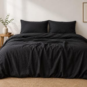 May include: A solid black duvet cover set featuring a textured fabric finish. The bedding includes a large duvet cover draped over a bed and two matching rectangular pillow shams positioned horizontally against the head of the bed frame.