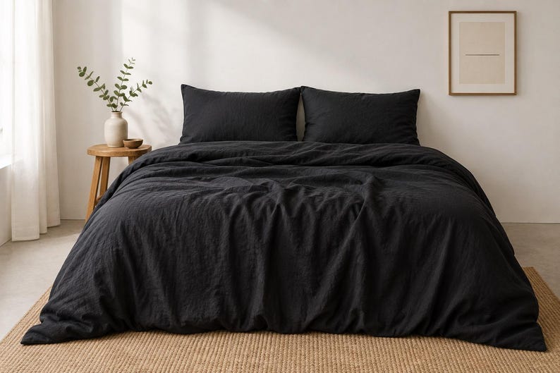 May include: A solid black duvet cover set featuring a textured fabric finish. The bedding includes a large duvet cover draped over a bed and two matching rectangular pillow shams positioned horizontally against the head of the bed frame.