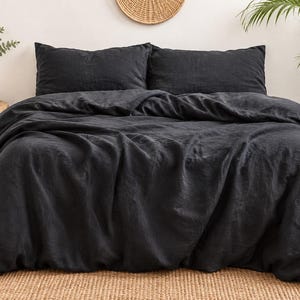 May include: A charcoal black duvet cover set featuring two matching rectangular pillowcases. The bedding has a textured, matte appearance with visible fabric folds and drapes across the bed, creating a soft and relaxed look for the bedroom.