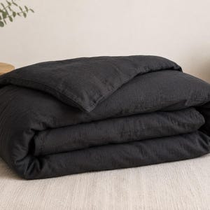 May include: A charcoal black duvet cover folded neatly into a rectangular shape. The fabric has a visible, slightly textured weave, suggesting a natural fiber construction. The duvet cover is layered with a single fold at the top edge.