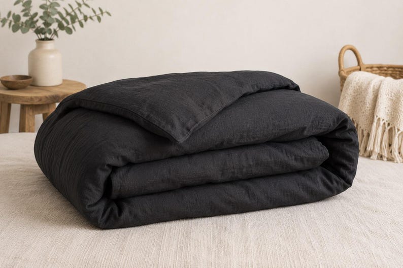 May include: A charcoal black duvet cover folded neatly into a rectangular shape. The fabric has a visible, slightly textured weave, suggesting a natural fiber construction. The duvet cover is layered with a single fold at the top edge.