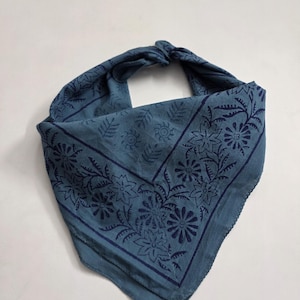 May include: A blue bandana with a floral pattern. The bandana is folded and tied at the top, showcasing the intricate dark blue floral design. The fabric has a soft, slightly wrinkled texture.
