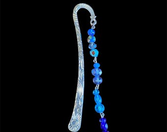 May include: Silver bookmark with a blue and purple beaded chain and a heart charm with a rainbow design.