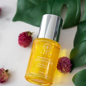 Puede incluir: Una botella de vidrio transparente con una tapa plateada llena de un líquido amarillo. La botella está etiquetada con "Gorgeous No.24 LUXURY ELIXIR with blend fruit & seed oil 1 oz. pure oil".