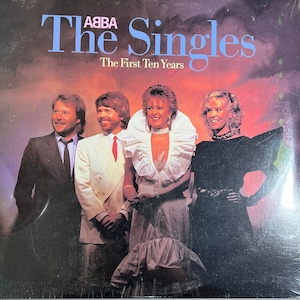 Puede incluir: La portada del álbum "The Singles: The First Ten Years" de ABBA muestra a los miembros de la banda con ropa formal. El título del álbum está en azul, con el nombre de la banda encima. El fondo es un degradado de naranja y morado.