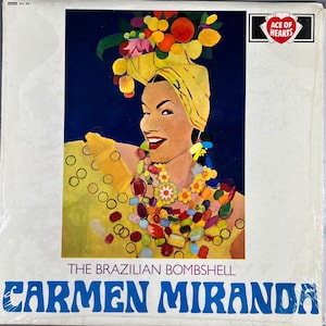 May include: Album cover featuring a vibrant illustration of Carmen Miranda. She wears a yellow turban adorned with fruit, a colorful necklace, and a yellow dress. The text reads "THE BRAZILIAN BOMBSHELL" and "CARMEN MIRANDA". The Ace of Hearts logo is in the upper right corner.