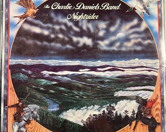 May include: Album cover for The Charlie Daniels Band's "Nightrider." The artwork features a landscape with mountains, clouds, and a full moon. Illustrations of a hawk, a duck, and two riders on horseback are also present. The album title is in a stylized font.