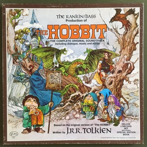 Puede incluir: Portada del álbum de la banda sonora original de El Hobbit. La ilustración presenta personajes y escenas de la historia, incluyendo un dragón, un mago y enanos. El álbum incluye diálogos, música y canciones. Escrito por J.R.R. Tolkien.