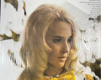 May include: Album cover for Tammy Wynette's "Another Lonely Song." The album art features a portrait of a woman with blonde hair, wearing a yellow bow. The album title and artist's name are at the top. The album is in a plastic sleeve.