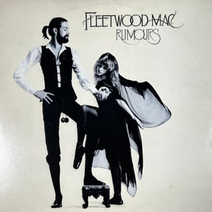 May include: Black and white album cover featuring the band Fleetwood Mac. The album title "Rumours" is displayed in elegant script. Two figures are posed, one standing with a yoyo, the other with a flowing shawl, standing on a small ornate stool.
