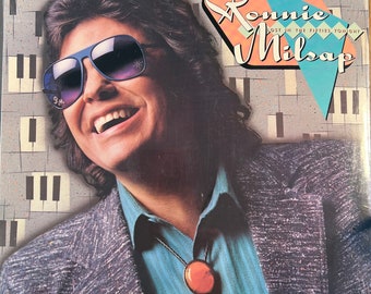 May include: A vintage record album cover featuring a portrait of Ronnie Milsap, a singer-songwriter, wearing sunglasses and a bolo tie. The album title is "Lost in the Fifties Tonight".