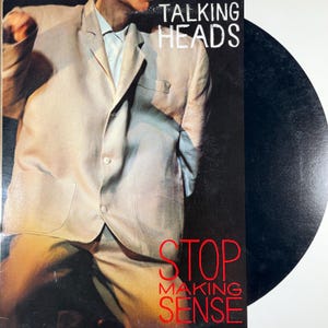 May include: Album cover for Talking Heads' "Stop Making Sense." The image shows a person in a light-coloured suit. The album title is in white text at the top, with "STOP MAKING SENSE" in red text at the bottom. A black vinyl record is visible.