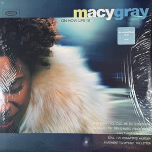 Può includere: Vinile sigillato dell'album di Macy Gray, intitolato "On How Life Is". La copertina dell'album presenta un primo piano del volto di una persona con un colletto di pelliccia soffice e di colore chiaro. Il titolo dell'album e il nome dell'artista sono in bianco e blu.