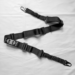 以下が含まれることがあります： 金属クリップと調節可能なストラップが付いた黒色のタクティカルスリング。 「ZEN DEVILS」の文字と中国語の文字が入ったスカルとクロスボーンのエンブレムが特徴です。 銃器を安全に運ぶように設計されています。