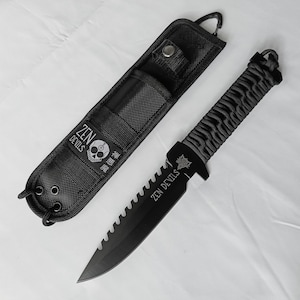 以下が含まれることがあります： 黒色の戦術ナイフ。ギザギザの刃とグレーと黒で包まれたハンドルが付いています。「ZEN DEVILS」の文字とスカルロゴが入った黒色の鞘に入っています。