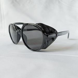 May include: Black sunglasses with dark lenses and side shields. The sunglasses have a thick, rounded frame and straight temples. The side shields are made of a textured material. The sunglasses are designed to protect the eyes from sunlight.