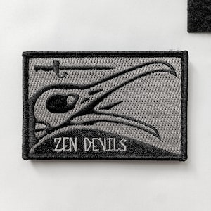 以下が含まれることがあります： スタイリッシュな鳥の頭のデザインと「ZEN DEVILS」の文字が刺繍されたグレーとブラックのワッペンです。