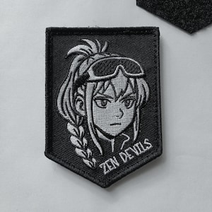 Peut inclure: Écusson brodé noir et blanc représentant un personnage de style anime avec des lunettes et une tresse. Le texte "ZEN DEVILS" est brodé en dessous. L'écusson est en forme de bouclier.