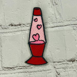 Może przedstawiać: Czerwono-różowa lampa lawowa z wzorem serca. Lampa jest wyszyta różowymi sercami.