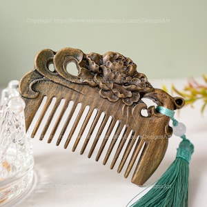 K&ouml;nnte beinhalten: Ein Kamm aus Holz mit einem geschnitzten Blumendesign und einem gr&uuml;nen Quasten. Der Kamm ist dunkelbraun und hat eine gl&auml;nzende Oberfl&auml;che. Das Blumendesign ist filigran und detailliert, und die Quaste ist aus weichem, seidenartigem Stoff.