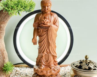 May include: A wooden statue of a Buddha holding a lotus flower in his hands. The statue is standing on a lotus base and is carved with intricate details. The statue is a light brown color.