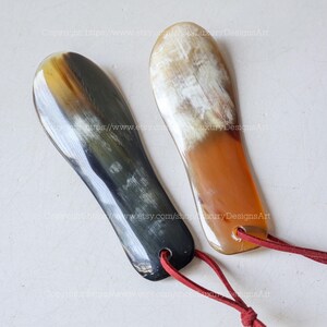 May include: Two horn shoe horns. One is dark with a yellow tip, the other is light with a brown tip. Both have a red cord attached for hanging. The shoe horns are smooth and curved.