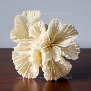May include: A cream-coloured, sculptural coral-like art piece. The intricate design features multiple layers of textured, petal-like structures. The artwork is displayed on a dark wooden surface against a light blue background. Copyright information is visible.
