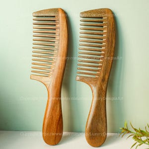May include: Two wooden combs with wide teeth are displayed. The combs are made of a light brown wood with a smooth finish. The handles are curved for easy grip. The combs are designed for detangling and styling hair.