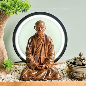 May include: A hand-carved wooden statue of a person in a seated meditation pose. The statue is made of dark brown wood and has a serene expression. The statue is sitting on a bed of white pebbles.