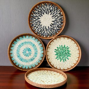 Puede incluir: Un conjunto de cuatro bandejas redondas decorativas con bordes de ratán tejido. Las bandejas presentan diseños intrincados en tonos azules, verdes y crema, que se asemejan a patrones florales. Las bandejas varían en tamaño y son adecuadas para la decoración del hogar.