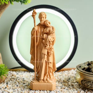 May include: A wooden statue of Saint Joseph holding a child. The statue is carved in a realistic style and has a warm, natural wood finish.