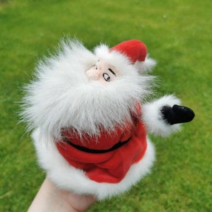 K&ouml;nnte beinhalten: Ein Pl&uuml;sch-Weihnachtsmann-Spielzeug mit wei&szlig;em Bart und rot-wei&szlig;er Kleidung. Das Spielzeug streckt seinen rechten Arm aus und tr&auml;gt einen schwarzen F&auml;ustling.