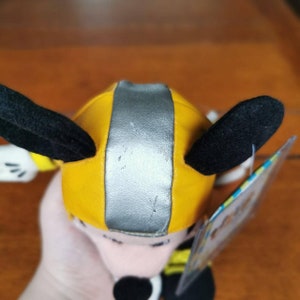 May include: A yellow and silver plush toy with black ears and a white face. The toy is wearing a yellow and silver helmet. The toy is a character from the Disney movie, "Planes".