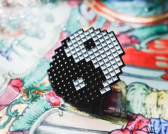 May include: A black and white yin yang symbol pin, made of small squares, on a colorful background.