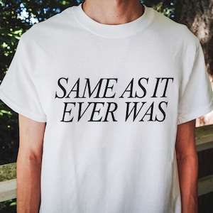 May include: White t-shirt with black text that reads "SAME AS IT EVER WAS".