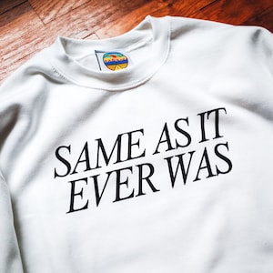 May include: White sweatshirt with black text that reads "SAME AS IT EVER WAS".