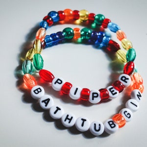 May include: Two colorful beaded bracelets with the names "Piper" and "Bath Tub" spelled out in white letters.