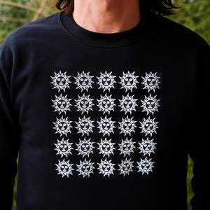 May include: Black sweatshirt featuring a repeating pattern of white sun-like faces. The design covers a large portion of the front of the sweatshirt. The sun faces have a smiling expression and spiky rays.
