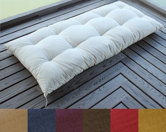 Puede incluir: Un cojín de banco rectangular de color blanco roto con una superficie acolchada suave y múltiples puntos de capitoné. El cojín presenta un diseño sencillo y limpio con lazos de tela visibles en las esquinas y una textura uniforme.