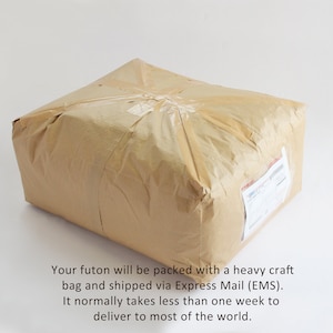 May include: A rectangular parcel wrapped in light brown craft paper and secured with clear adhesive tape. A white shipping label with a barcode and text is attached to the side of the package. The package has a creased and textured surface.