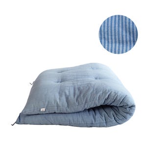 Puede incluir: Un colchón futón a rayas azules y blancas. El colchón está doblado, revelando un diseño acolchado con botones. Un primer plano muestra la textura de la tela. El futón es una opción de ropa de cama suave y cómoda.