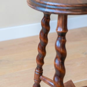 May include: A round wooden stool with a dark brown finish, featuring three distinctively twisted, spiral-shaped legs that connect to a central triangular support base. The stool has a smooth, circular top with a slightly rounded edge profile.