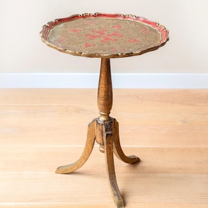 May include: A vintage side table with a round, scalloped top featuring a red and gold floral design. The table has a wooden pedestal base and three curved legs. The table is approximately 28 inches tall.