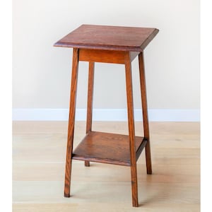 Op de afbeelding: Een kleine, antieke houten bijzettafel met een rechthoekig blad en een onderste plank. De tafel is gemaakt van donkerbruin hout en heeft een eenvoudig, elegant ontwerp. De tafel is ongeveer 76 cm hoog.