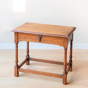 May include: An antique wooden table with a rectangular top and a single drawer. The table is made of light brown wood and features turned legs and a decorative brass pull on the drawer. The table is approximately 71 cm long, 46 cm wide, and 71 cm high.