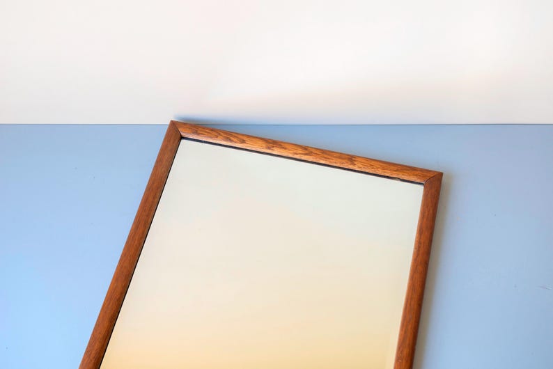 May include: A rectangular wall mirror featuring a warm-toned wooden frame with a visible grain pattern. The mirror glass is clear and reflective, set within the simple, clean-lined wooden border that surrounds the entire perimeter of the piece.