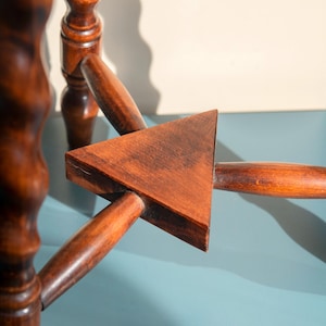 May include: A brown wooden stool base featuring three spiraled legs connected by a central triangular support piece. The legs are cylindrical with a twisted design, and the horizontal supports meet at a flat, solid wood triangle in the center.